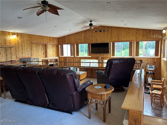 living room with ceiling fan, a textured ceiling, hardwood / wood-style floors, wooden walls, and vaulted ceiling