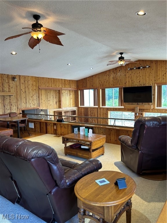 carpeted living room featuring wood walls, a textured ceiling, lofted ceiling, and ceiling fan