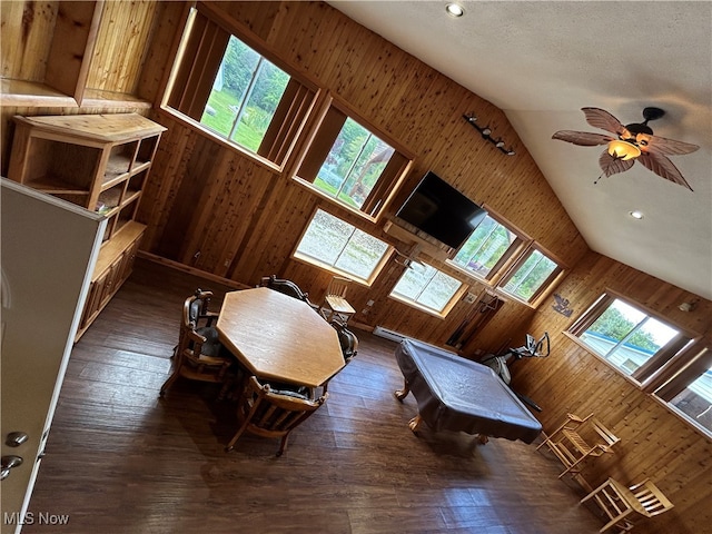 unfurnished living room with dark hardwood / wood-style flooring, wood walls, vaulted ceiling, and ceiling fan