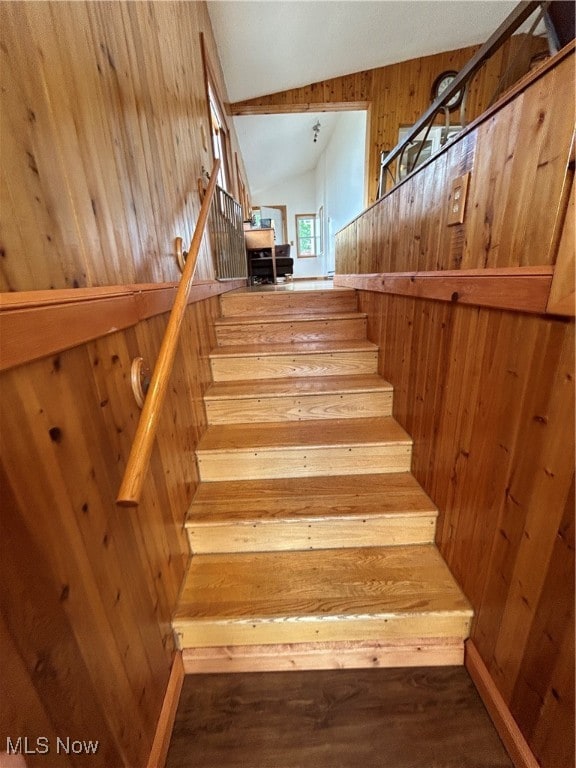 staircase with wood walls, hardwood / wood-style flooring, and vaulted ceiling