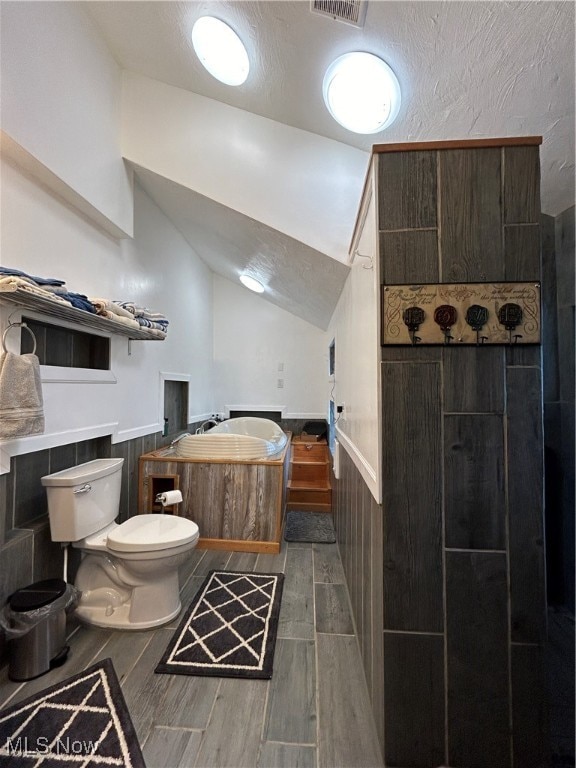 bathroom featuring hardwood / wood-style floors, wood walls, toilet, and vaulted ceiling