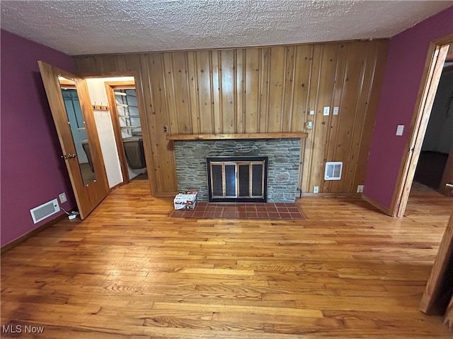 unfurnished living room with a stone fireplace, light wood-type flooring, wooden walls, and a textured ceiling