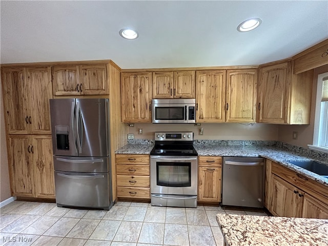 kitchen featuring stainless steel appliances, light tile patterned floors, sink, and light stone countertops