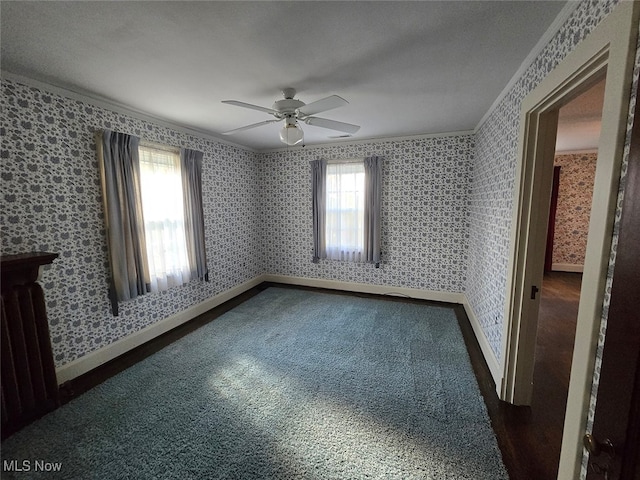 empty room with ceiling fan, a healthy amount of sunlight, dark colored carpet, and ornamental molding