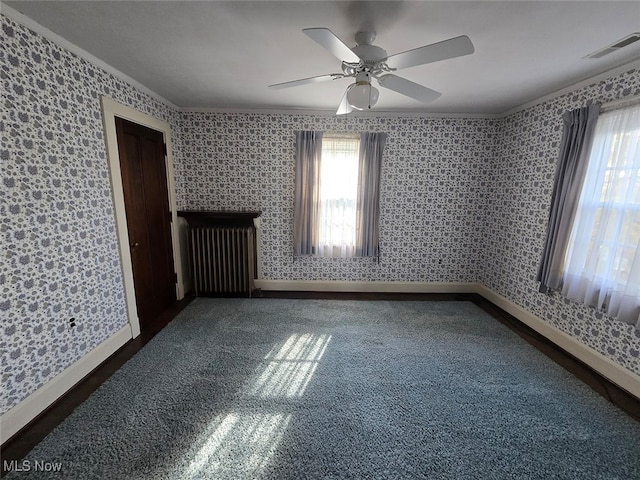 empty room featuring ornamental molding, dark colored carpet, ceiling fan, and radiator