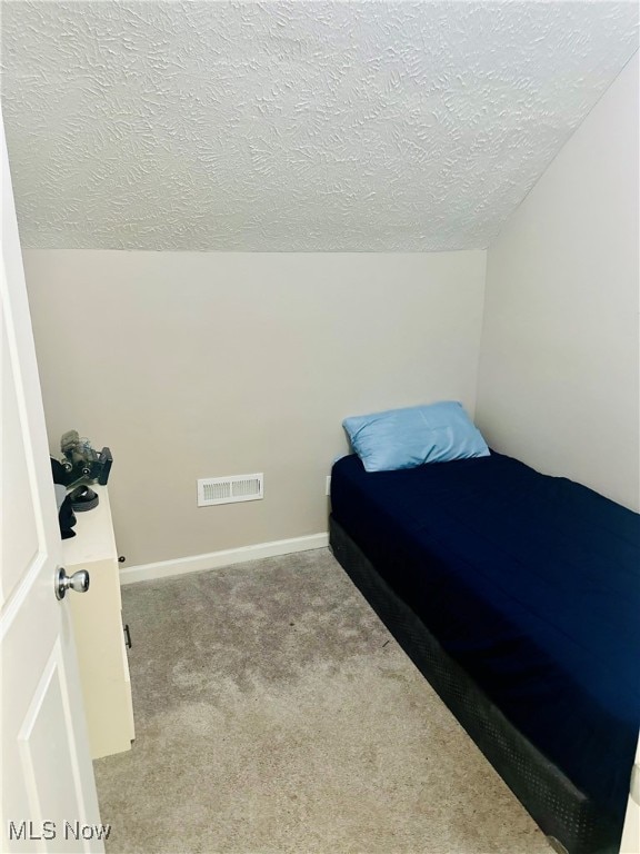 bedroom featuring light carpet, a textured ceiling, and lofted ceiling