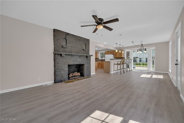 unfurnished living room with a fireplace, ceiling fan with notable chandelier, and light wood-type flooring