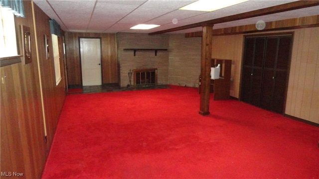 basement featuring wood walls, a fireplace, carpet, and a drop ceiling