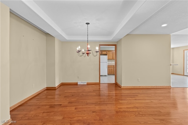 spare room with a tray ceiling, a chandelier, and light hardwood / wood-style floors