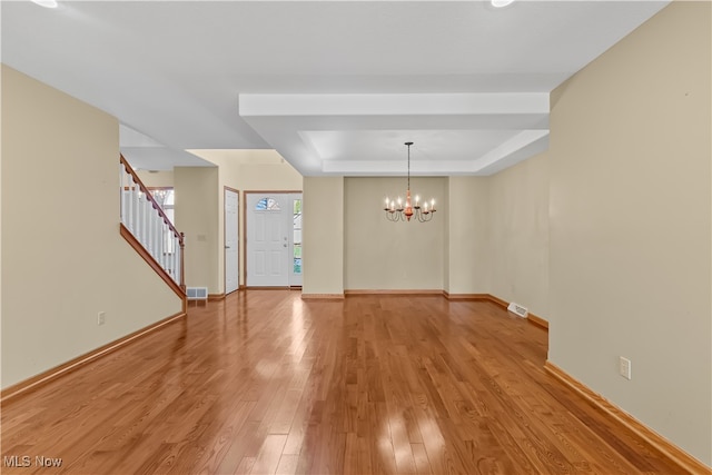 spare room featuring a tray ceiling, a notable chandelier, and light wood-type flooring