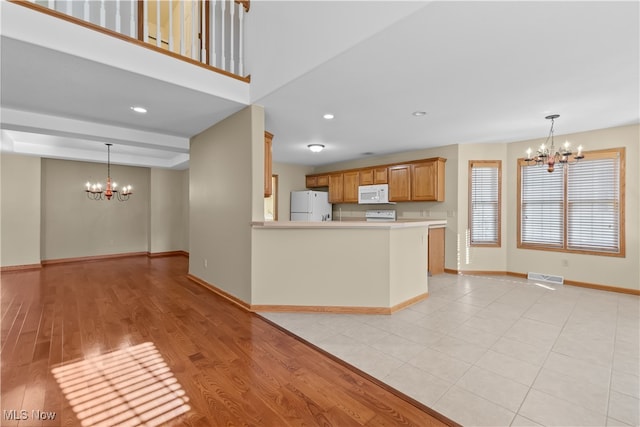 kitchen with white appliances, decorative light fixtures, light hardwood / wood-style floors, kitchen peninsula, and a chandelier