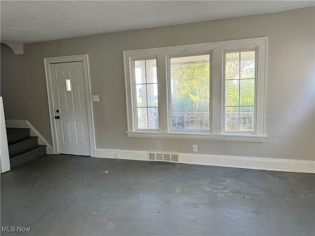 foyer entrance featuring visible vents, unfinished concrete flooring, a textured ceiling, stairway, and baseboards