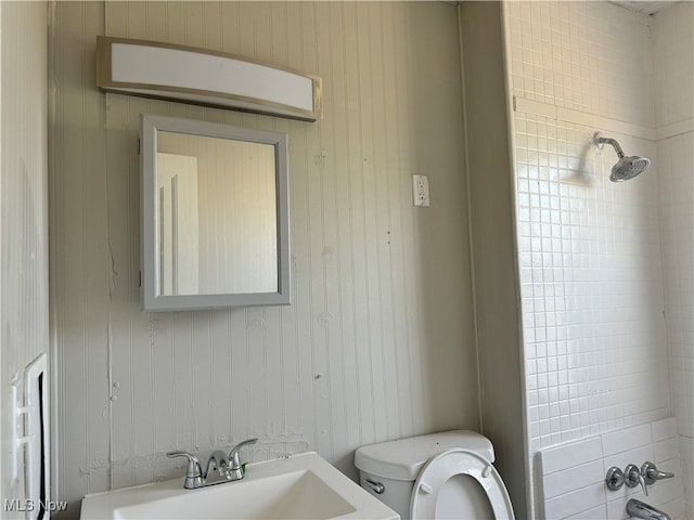 bathroom with wooden walls, sink, a tile shower, and toilet