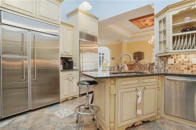 kitchen with stainless steel appliances, cream cabinets, kitchen peninsula, sink, and tasteful backsplash