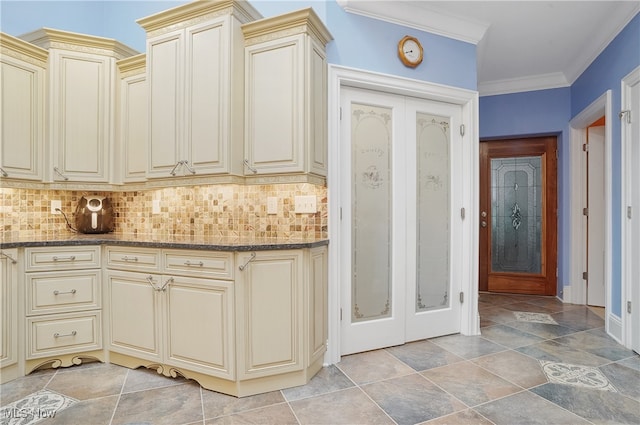 kitchen with dark stone countertops, tasteful backsplash, cream cabinets, and ornamental molding