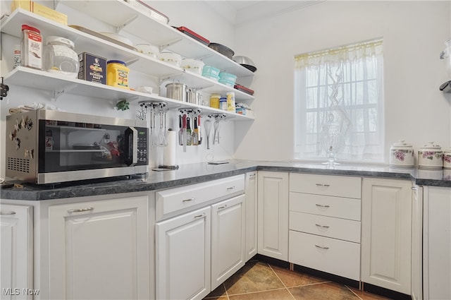 kitchen featuring white cabinets, ornamental molding, and dark tile patterned floors