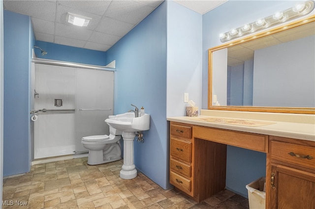 bathroom featuring a paneled ceiling, sink, toilet, and a shower with shower door