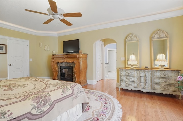 bedroom with a fireplace, ceiling fan, light wood-type flooring, and ornamental molding