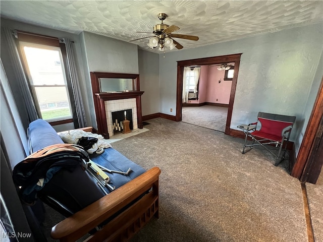 living room with ceiling fan, a tiled fireplace, a textured ceiling, and carpet floors