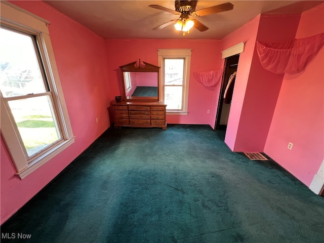 unfurnished bedroom with a closet, ceiling fan, multiple windows, and dark carpet