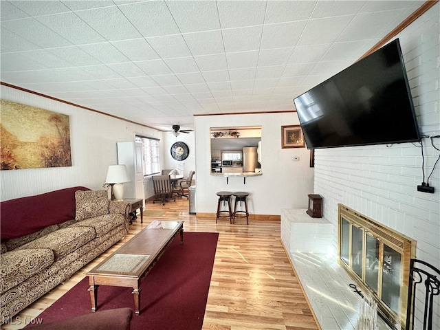 living room with ornamental molding, a brick fireplace, hardwood / wood-style floors, and ceiling fan