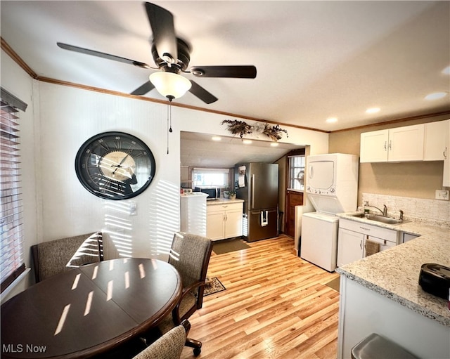 kitchen with stacked washing maching and dryer, sink, white cabinets, stainless steel appliances, and crown molding