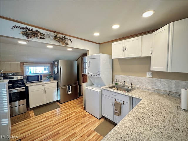 kitchen with sink, white cabinetry, stainless steel appliances, stacked washer / dryer, and light hardwood / wood-style floors