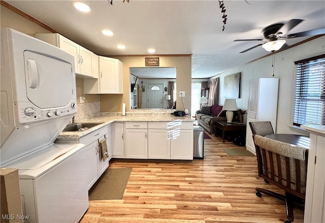 kitchen with stacked washer / drying machine, crown molding, light hardwood / wood-style flooring, ceiling fan, and white cabinets