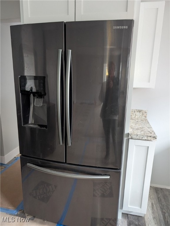 details featuring white cabinets, stainless steel fridge with ice dispenser, light hardwood / wood-style flooring, and light stone counters