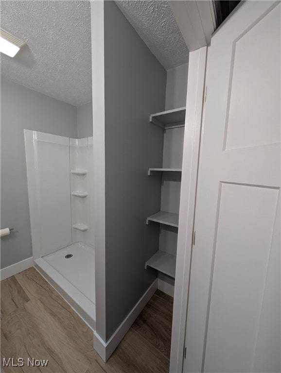 interior space featuring wood-type flooring, a textured ceiling, and walk in shower