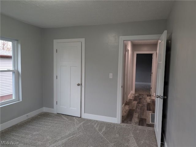 unfurnished bedroom featuring dark colored carpet and a textured ceiling