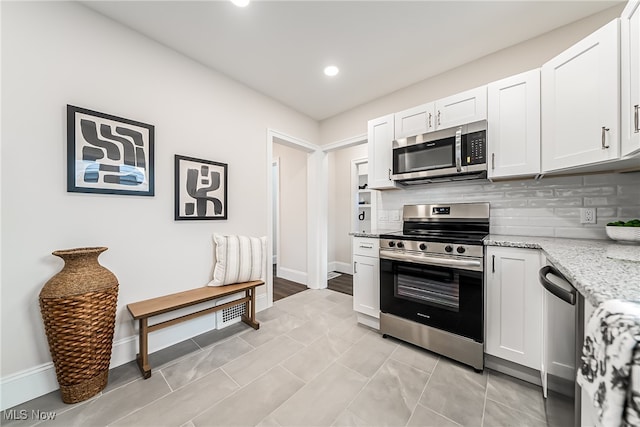 kitchen with tasteful backsplash, light tile patterned flooring, stainless steel appliances, light stone countertops, and white cabinets