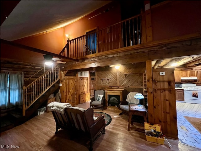 living room featuring wood walls, hardwood / wood-style floors, ceiling fan, and a towering ceiling