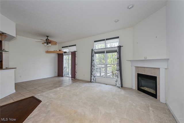 unfurnished living room with ceiling fan, a tile fireplace, a textured ceiling, and light colored carpet