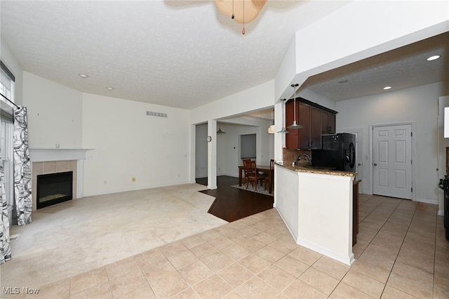 kitchen featuring a tiled fireplace, black refrigerator, a textured ceiling, light carpet, and ceiling fan