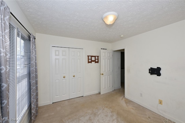 unfurnished bedroom featuring light colored carpet, a textured ceiling, and a closet