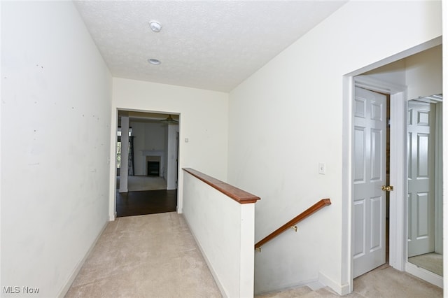 hallway with a textured ceiling and light carpet