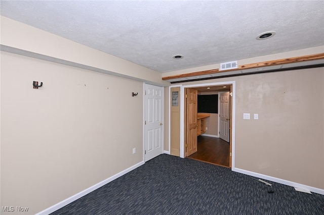 unfurnished room with a textured ceiling and dark colored carpet