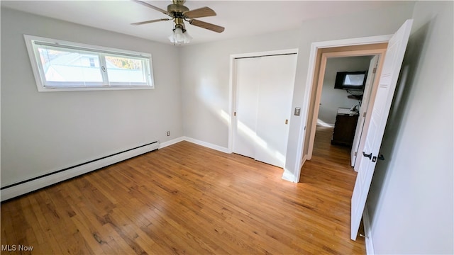 unfurnished bedroom featuring baseboard heating, light wood-type flooring, ceiling fan, and a closet