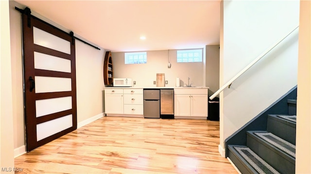 bar featuring white cabinetry, light wood-type flooring, a barn door, and stainless steel refrigerator