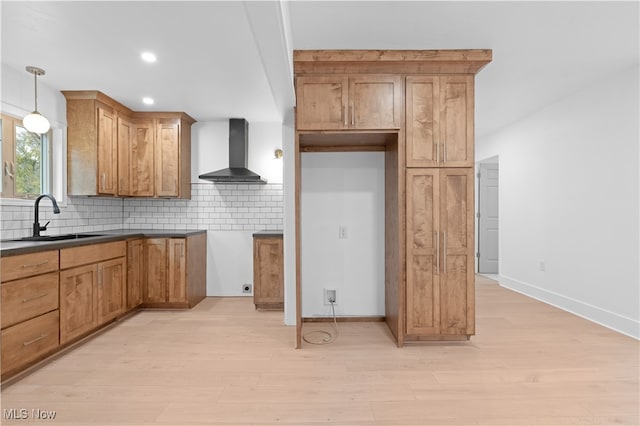 kitchen with wall chimney range hood, backsplash, hanging light fixtures, sink, and light hardwood / wood-style floors