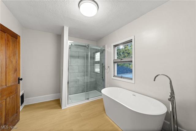 bathroom featuring plus walk in shower, wood-type flooring, and a textured ceiling