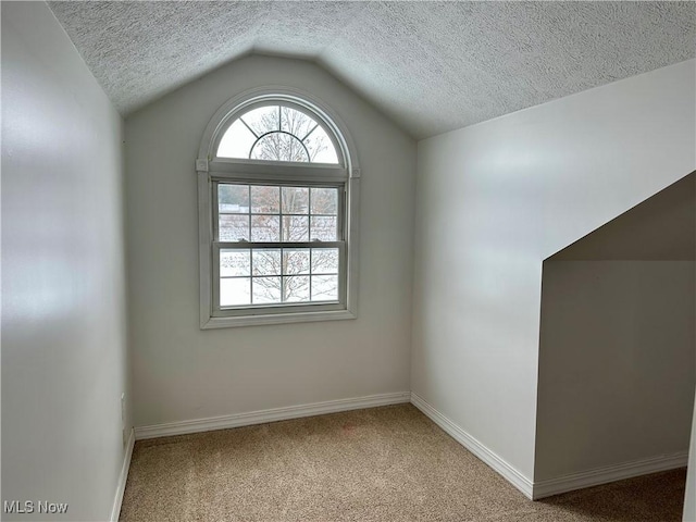 carpeted spare room featuring a textured ceiling and lofted ceiling