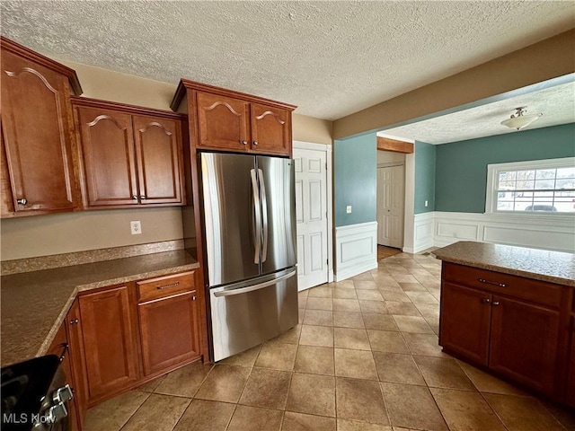 kitchen featuring light tile patterned floors, range, a textured ceiling, and stainless steel refrigerator