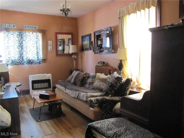 living room featuring wood-type flooring, heating unit, plenty of natural light, and an inviting chandelier