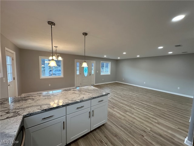 kitchen with white cabinets, hardwood / wood-style floors, hanging light fixtures, and light stone countertops