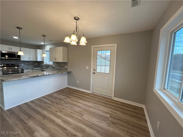 kitchen featuring white cabinetry, kitchen peninsula, stainless steel appliances, and tasteful backsplash