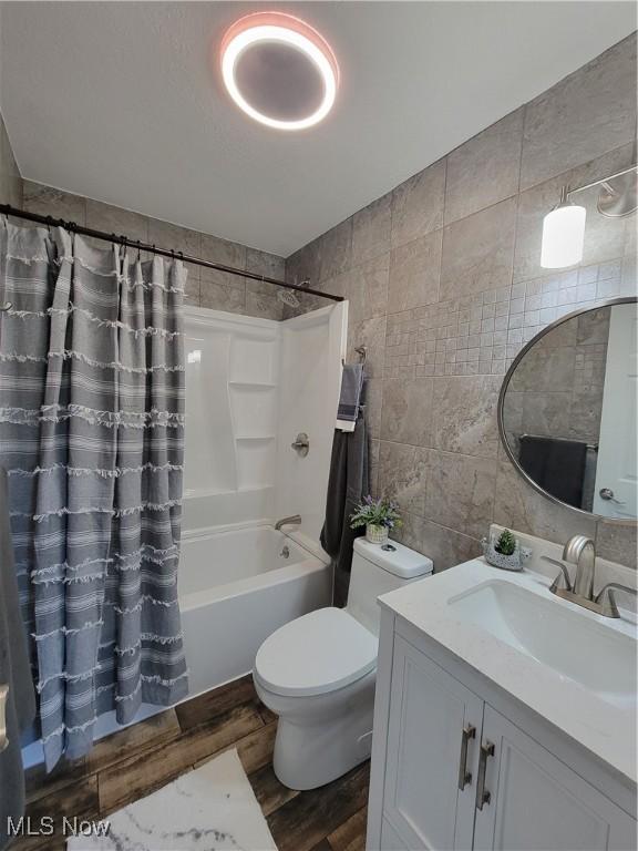 full bathroom featuring hardwood / wood-style floors, toilet, shower / bath combo with shower curtain, vanity, and tile walls