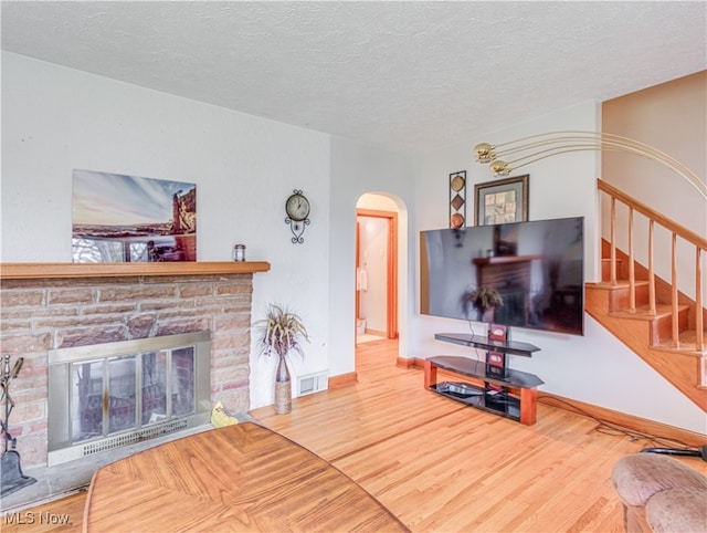 living room featuring a stone fireplace, wood-type flooring, and a textured ceiling