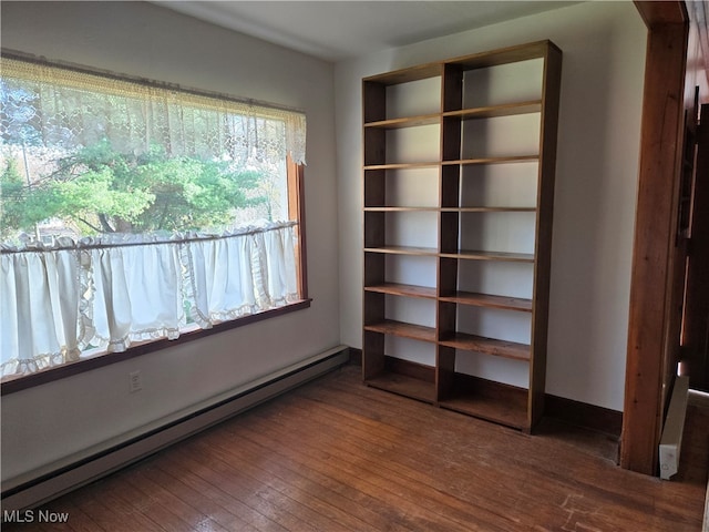 unfurnished bedroom featuring a baseboard heating unit and dark wood-type flooring